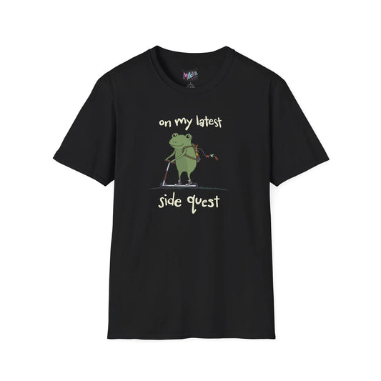 Black t-shirt with a cute green frog on a scooter, wearing a backpack that is slightly unzipped with small items hanging out. Text reads, "on my latest side quest." Whimsical and playful design.