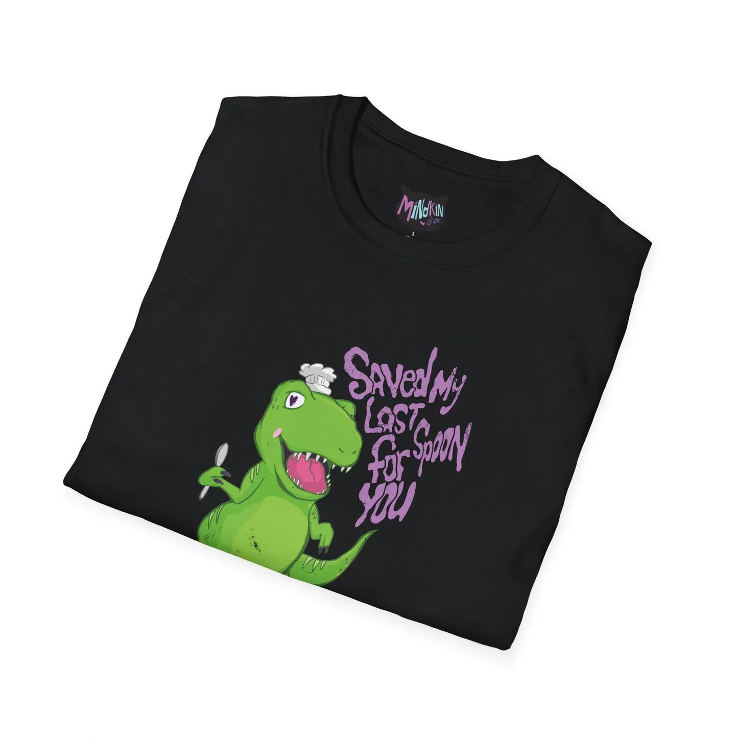 Folded black t-shirt with a cartoon green dinosaur holding a spoon and wearing a chef hat. Purple text reads "Saved my last spoon for you." Playful tone.