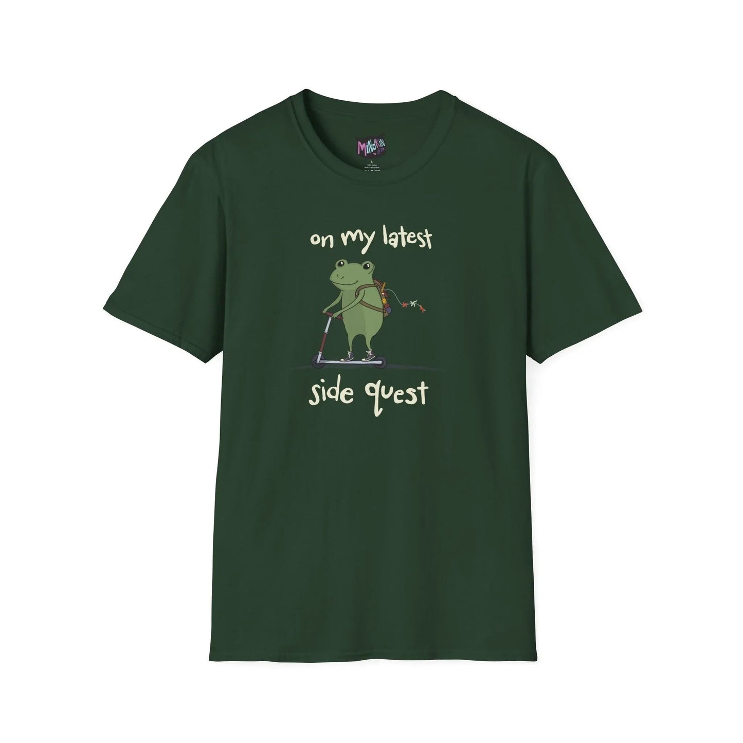 Green t-shirt with a cute green frog on a scooter, wearing a backpack that is slightly unzipped with small items hanging out. Text reads, "on my latest side quest." Whimsical and playful design.