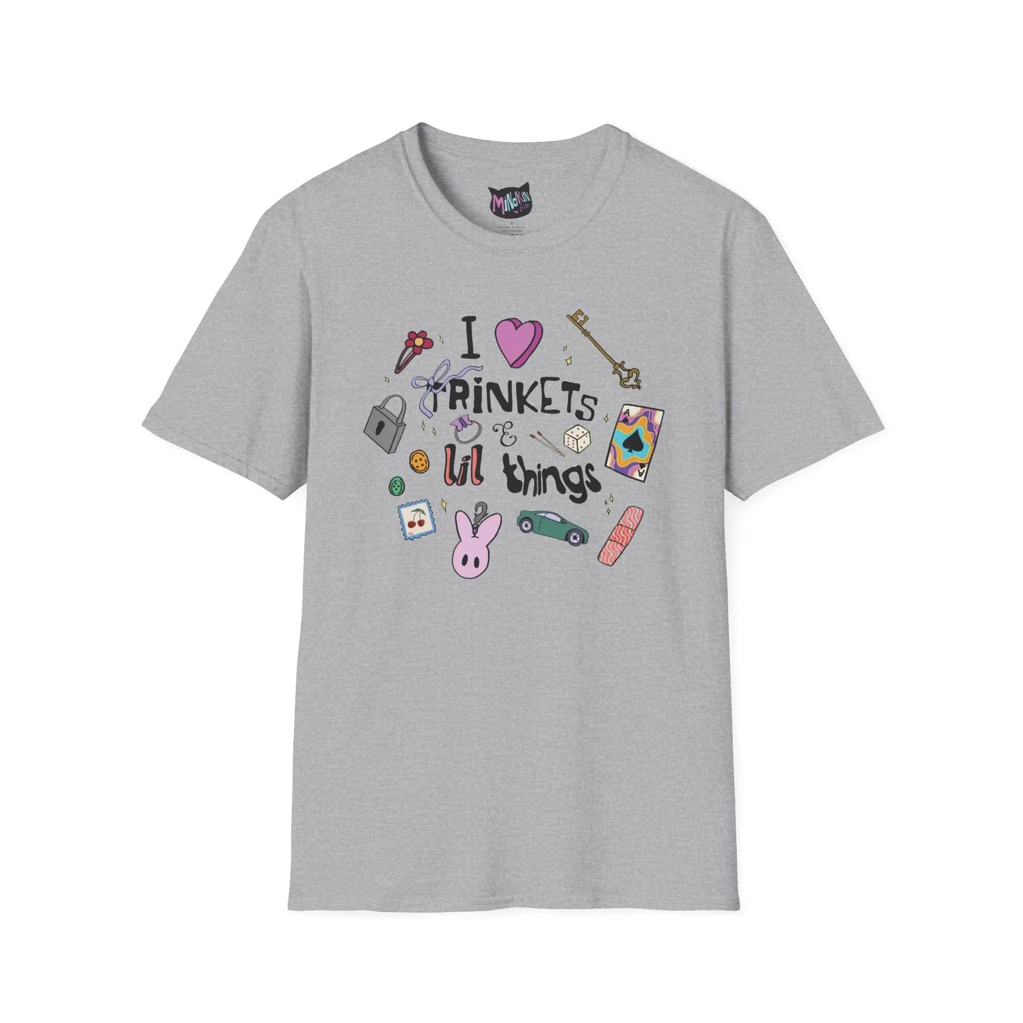 Gray T-shirt featuring doodles of ornate keys, dice, a toy car, a flower hairclip, a postage stamp, a butterfly ring, and a pink bunny keychain. Text reads "I love trinkets and lil things" with playful, colorful illustrations.