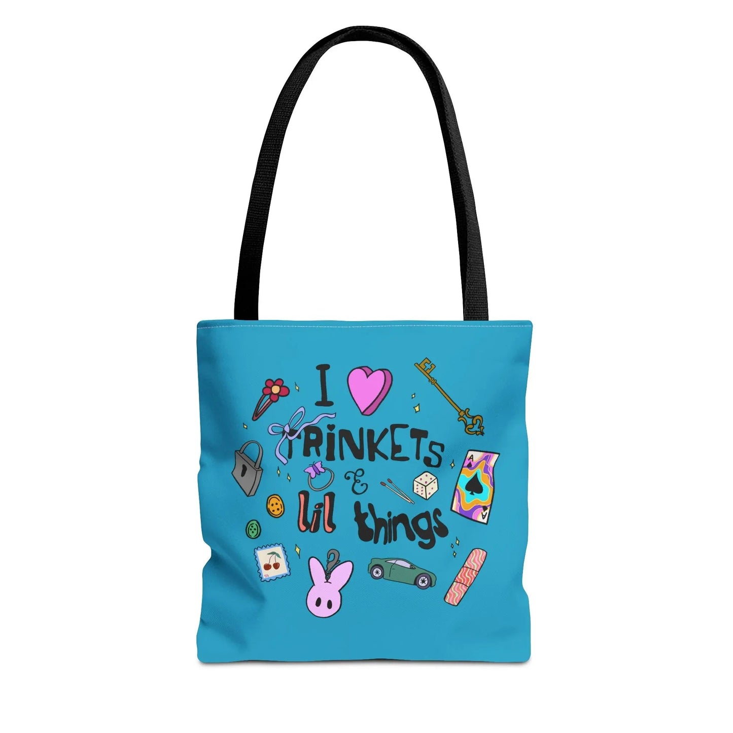Blue tote bag with black handles, featuring playful doodles like a key, ribbon, dice, and cartoon bunny. Text reads "I love trinkets & lil things." Fun and whimsical.