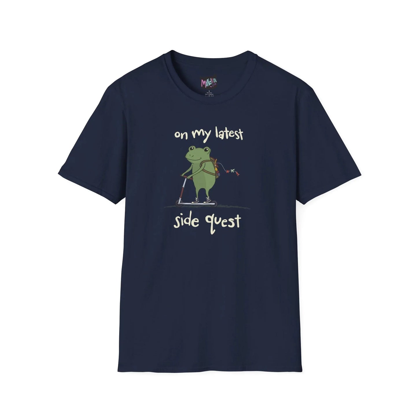 Navy t-shirt with a cute green frog on a scooter, wearing a backpack that is slightly unzipped with small items hanging out. Text reads, "on my latest side quest." Whimsical and playful design.