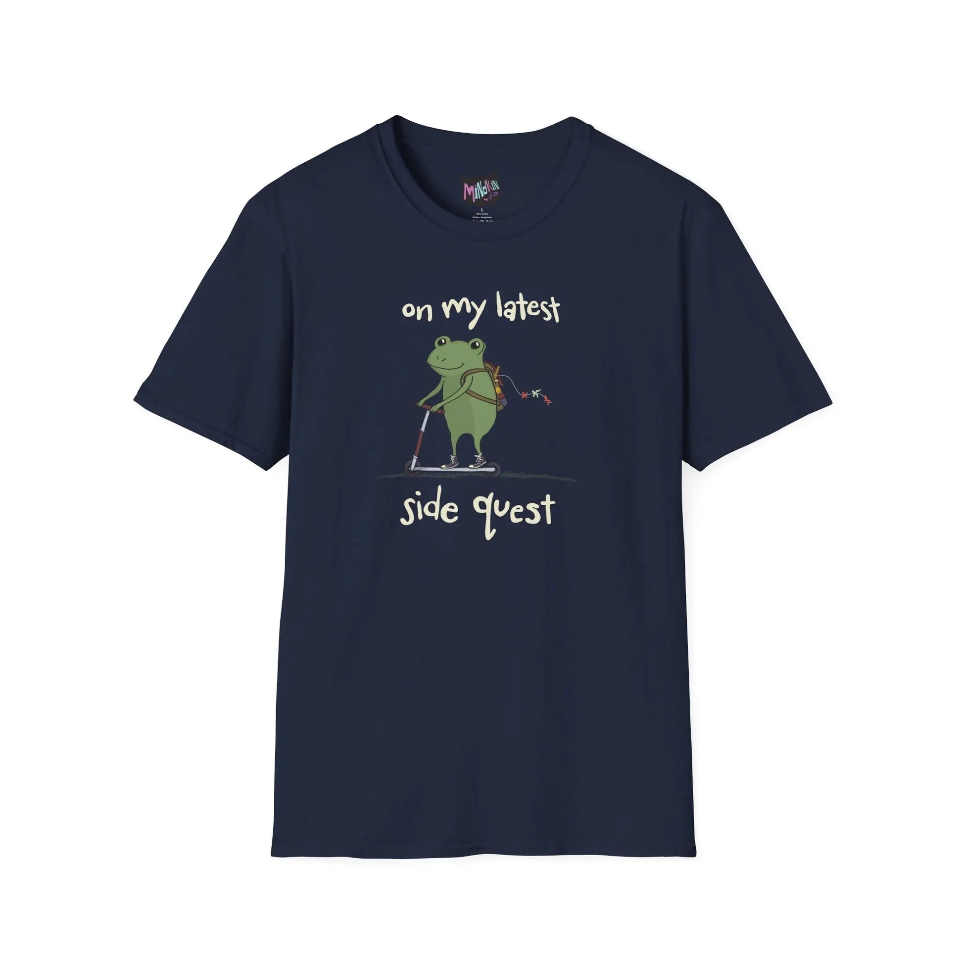 Navy t-shirt with a cute green frog on a scooter, wearing a backpack that is slightly unzipped with small items hanging out. Text reads, "on my latest side quest." Whimsical and playful design.
