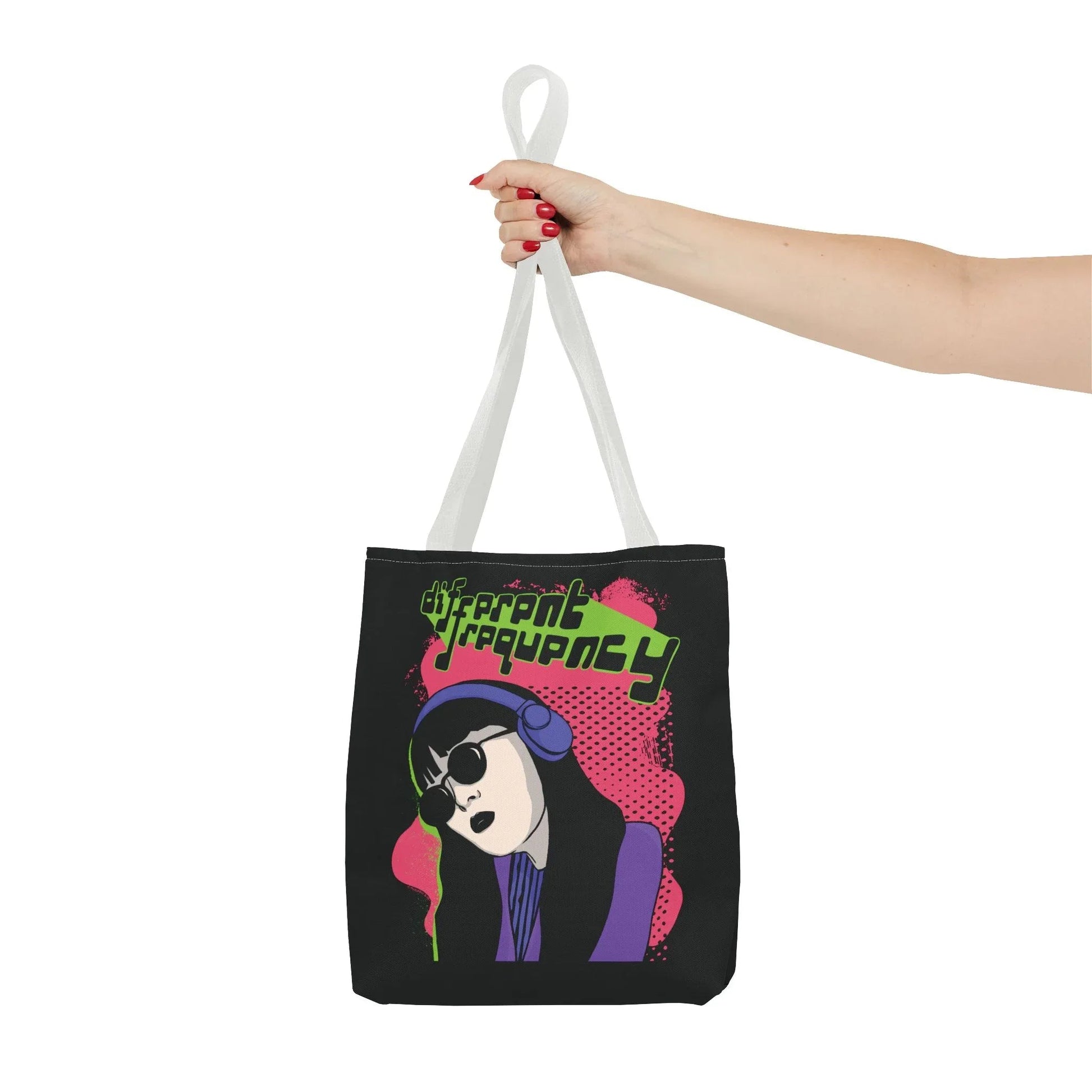 A hand holds a tote bag with durable,  reinforced white straps. The bag features a colorful illustration of a woman with headphones and sunglasses, with the text "Different Frequency" in neon green.