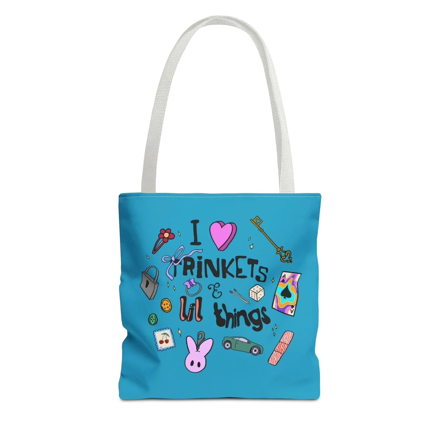 Blue tote bag with white handles, featuring playful doodles like a key, ribbon, dice, and cartoon bunny. Text reads "I love trinkets & lil things." Fun and whimsical.