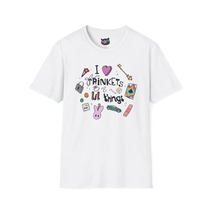 White T-shirt featuring doodles of ornate keys, dice, a toy car, a flower hairclip, a postage stamp, a butterfly ring, and a pink bunny keychain. Text reads "I love trinkets and lil things" with playful, colorful illustrations.