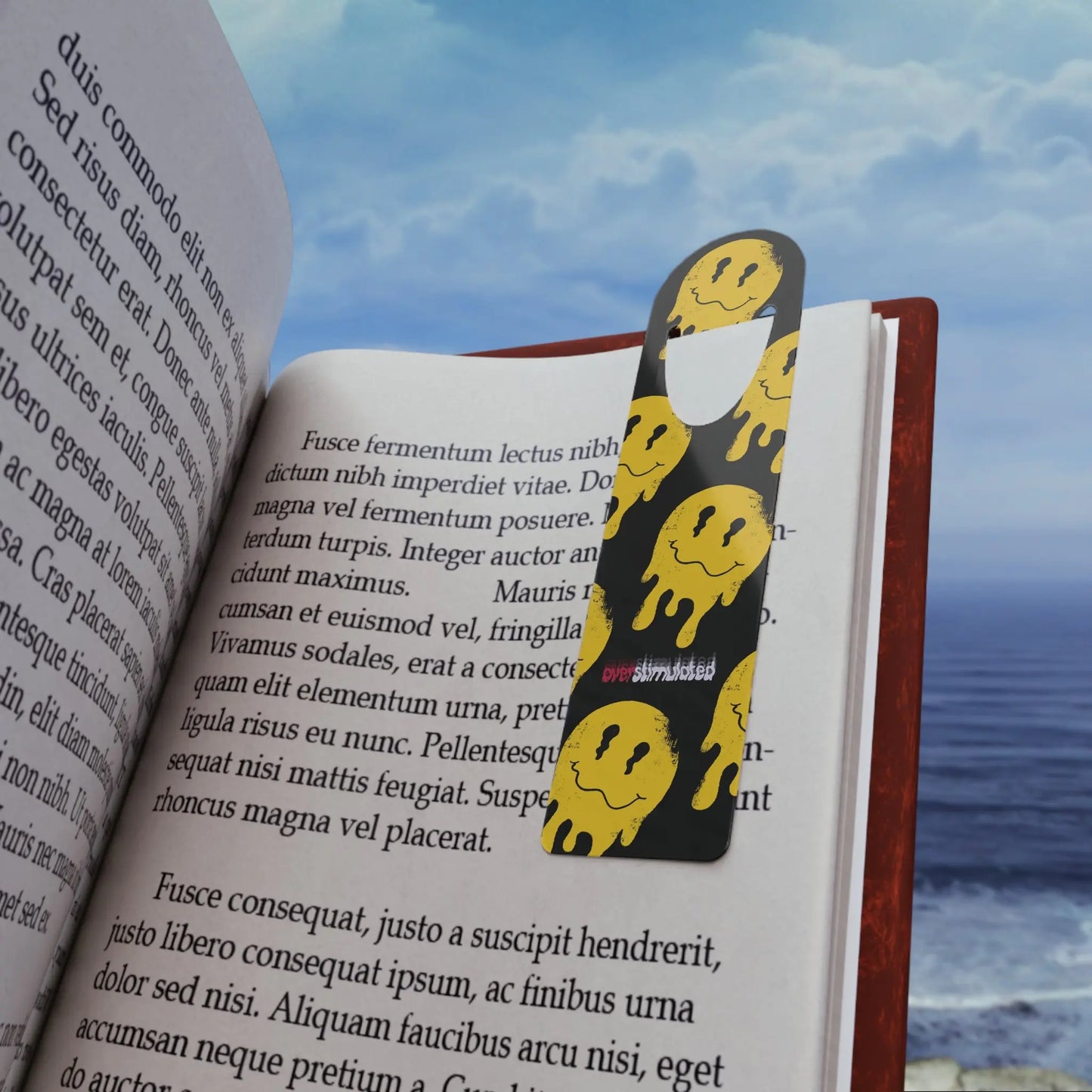 Open book with a bookmark featuring yellow, melting smiley faces on a black background, set against a serene ocean and sky backdrop.