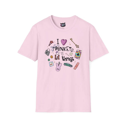 Pink T-shirt featuring doodles of ornate keys, dice, a toy car, a flower hairclip, a postage stamp, a butterfly ring, and a pink bunny keychain. Text reads "I love trinkets and lil things" with playful, colorful illustrations.