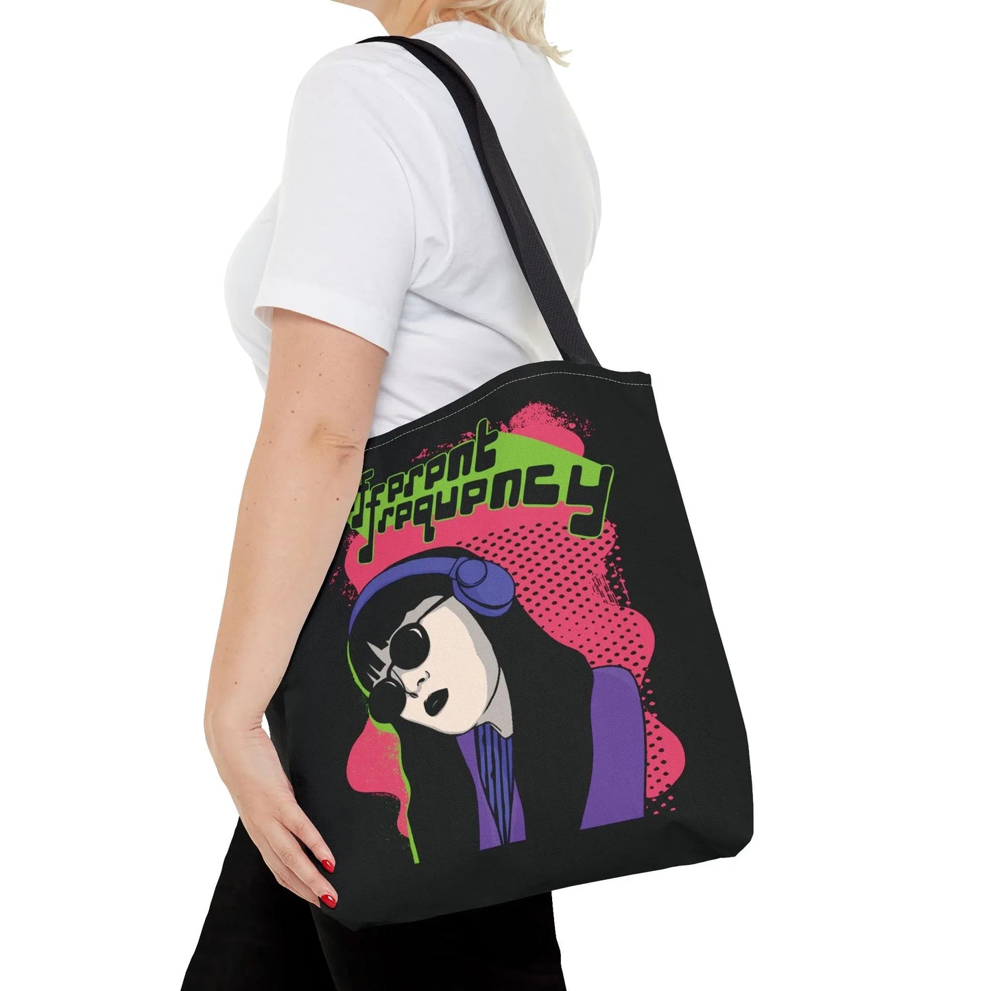 A person carries a black tote bag featuring colorful pop art of a woman wearing purple with headphones. Bold neon green text reads "Different Frequency" over pink.