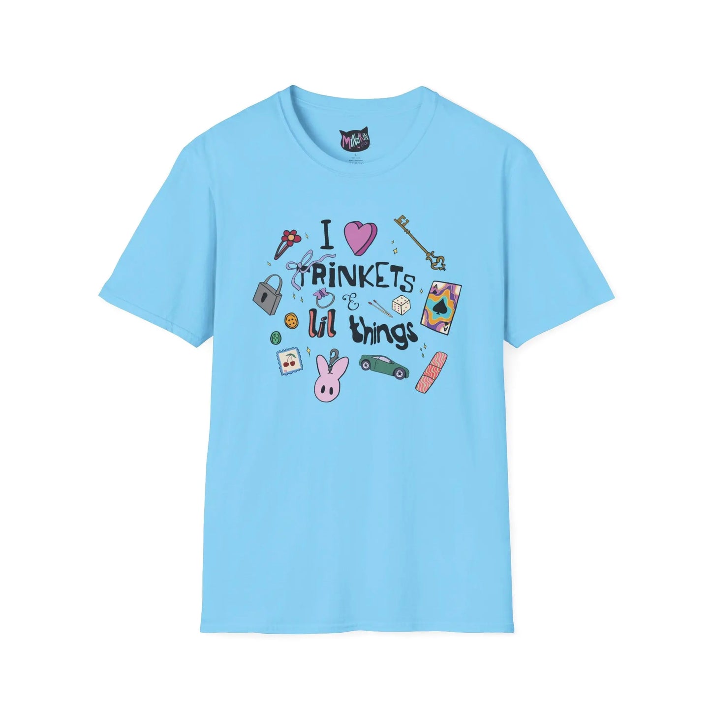 Blue T-shirt featuring doodles of ornate keys, dice, a toy car, a flower hairclip, a postage stamp, a butterfly ring, and a pink bunny keychain. Text reads "I love trinkets and lil things" with playful, colorful illustrations.