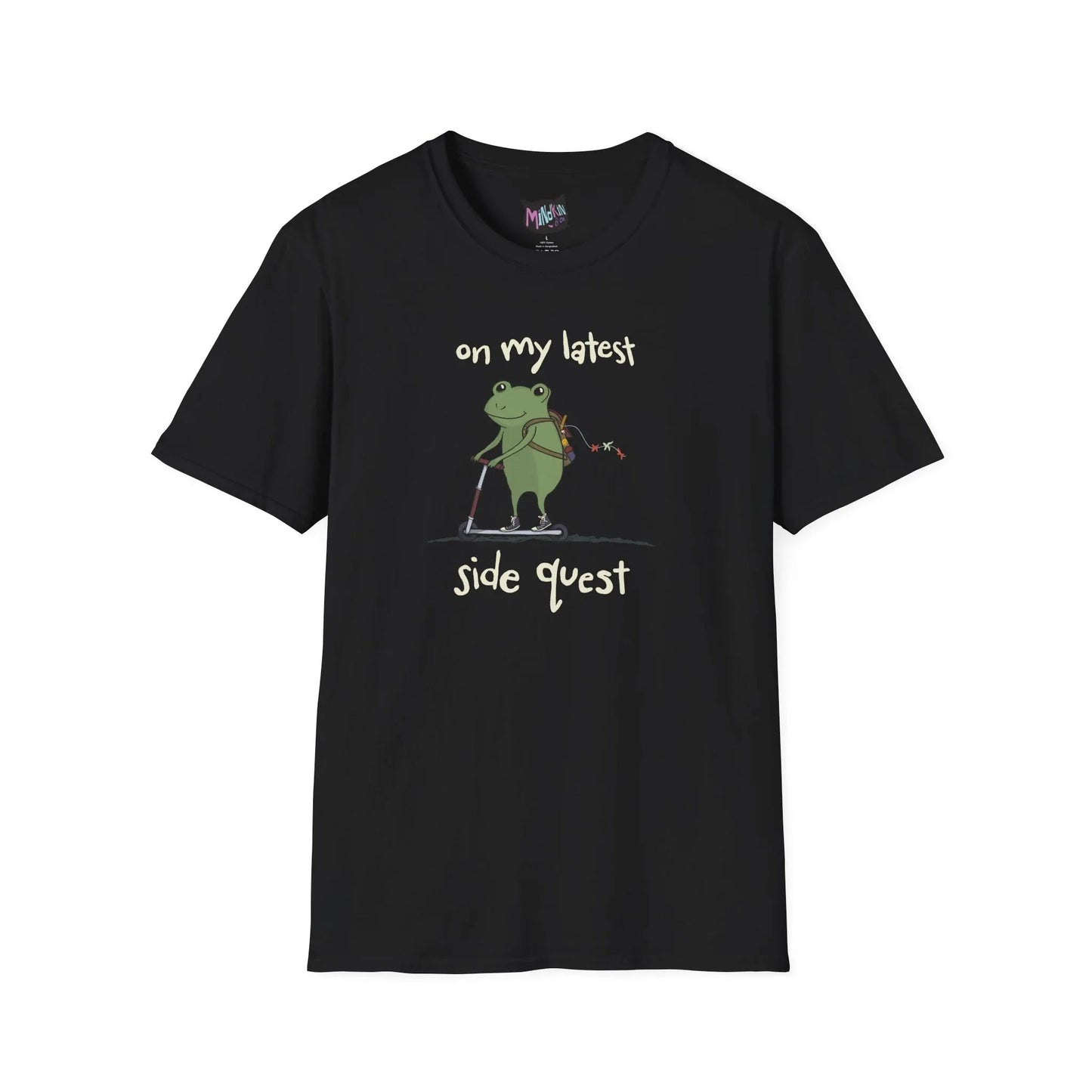 Black t-shirt with a cute green frog on a scooter, wearing a backpack that is slightly unzipped with small items hanging out. Text reads, "on my latest side quest." Whimsical and playful design.