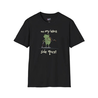 Black t-shirt with a cute green frog on a scooter, wearing a backpack that is slightly unzipped with small items hanging out. Text reads, "on my latest side quest." Whimsical and playful design.