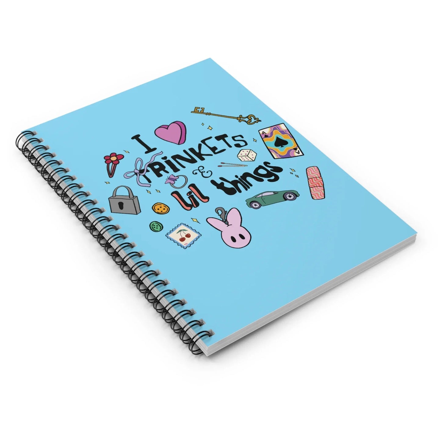 Spiral notebook with a blue cover featuring playful doodles and the phrase "I love trinkets & lil things." Metal spiral binding lays flat to indicate easy on-the-go writing.