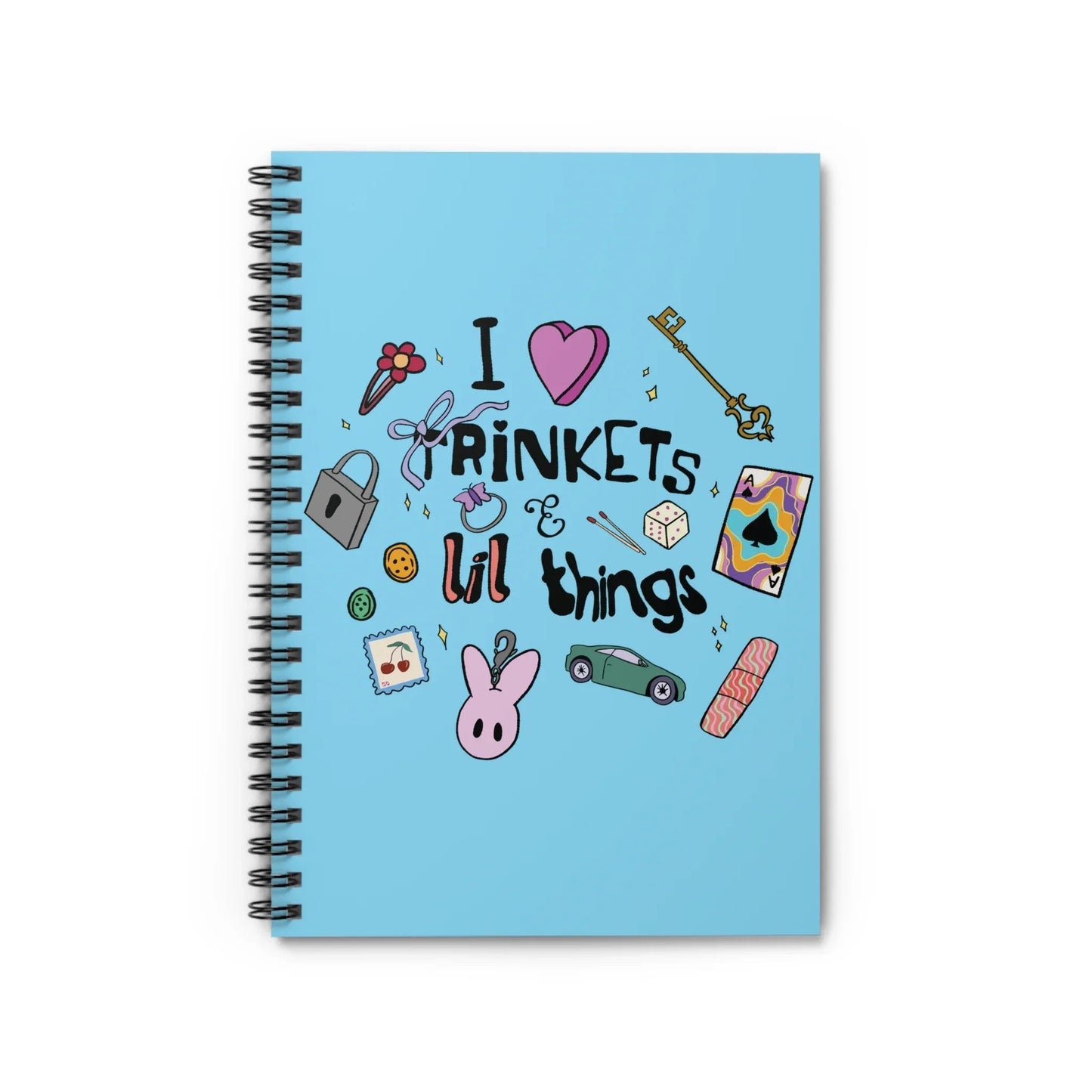 Blue notebook cover with playful illustrations, including a heart, key, dice, flower, and text: "I love trinkets & lil things." Whimsical and fun design.
