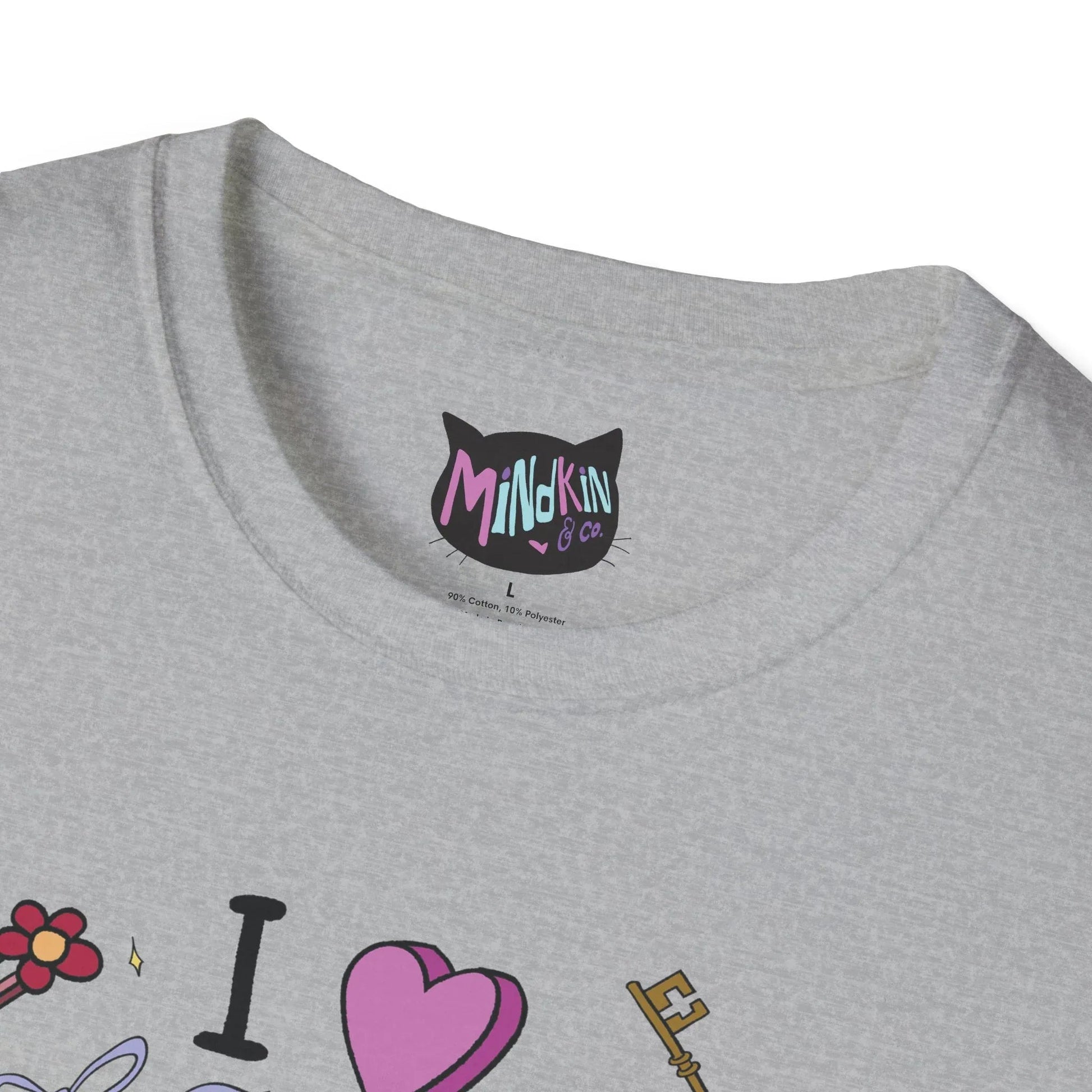 Close-up of a gray t-shirt's ribbed collar neckline showing a black cat-shaped label with "Mindkin & Co" in colorful text. Below are playful illustrations of a flower hairclip, "I ♥️" and a key.