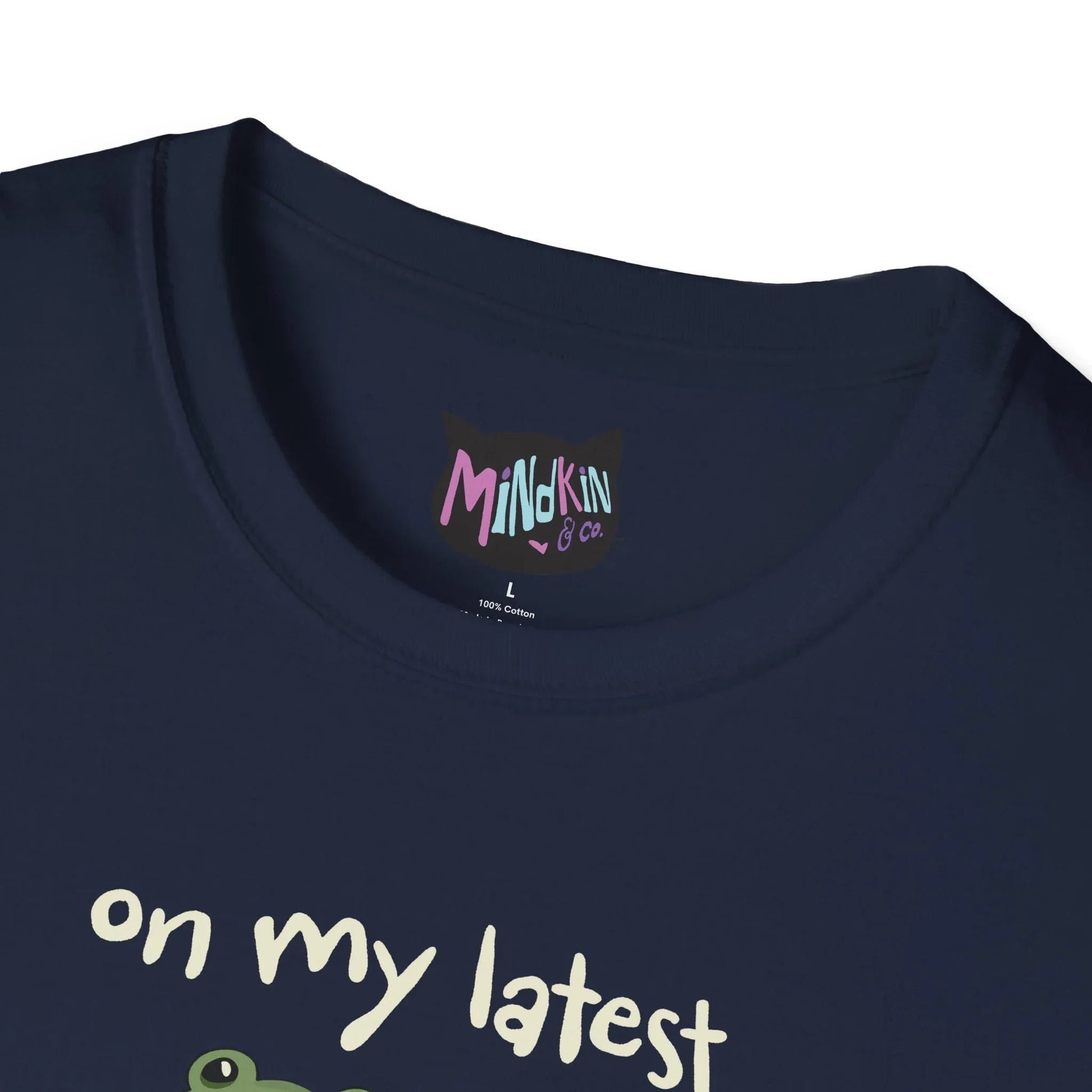 Close-up of a navy T-shirt ribbed collar with colorful "Mindkin & Co." label. The visible text "on my latest" is printed in white, suggesting playful humor.