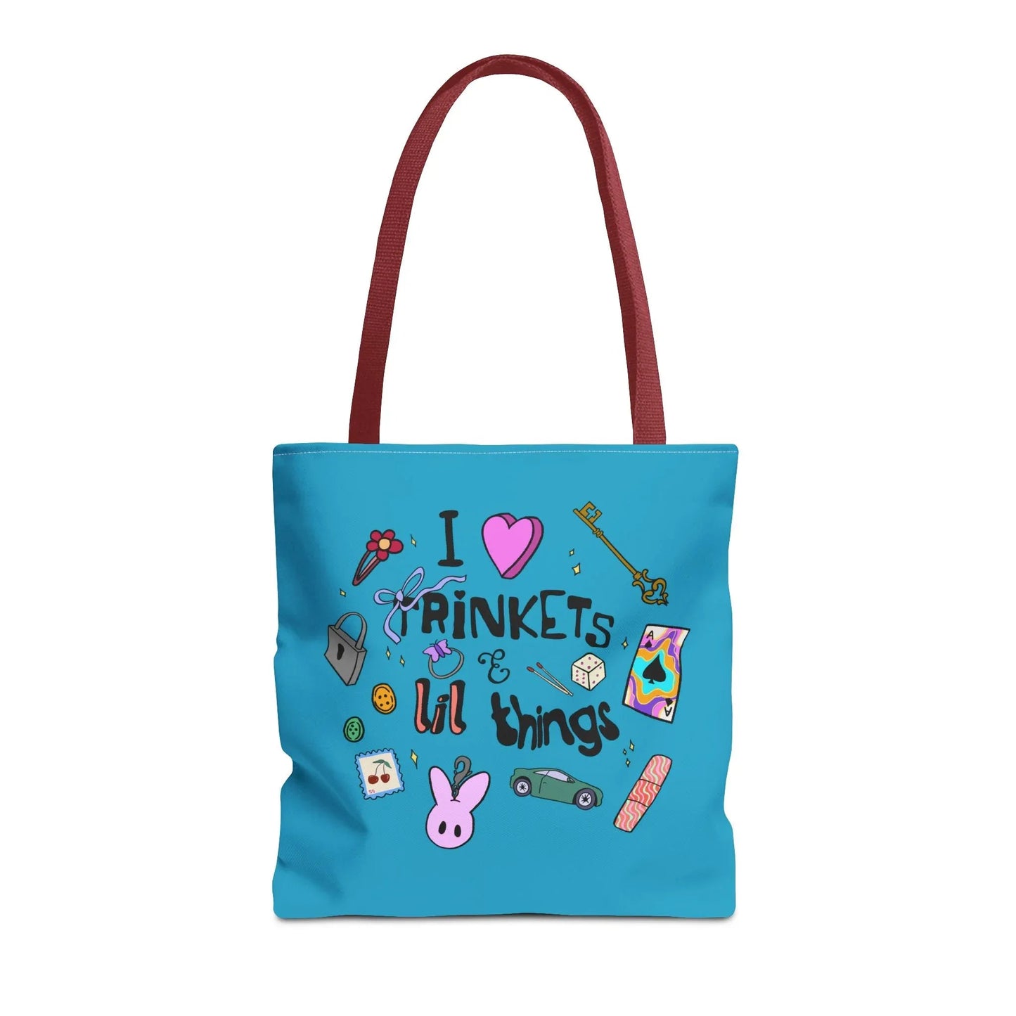 Blue tote bag with red handles, featuring playful doodles like a key, ribbon, dice, and cartoon bunny. Text reads "I love trinkets & lil things." Fun and whimsical.