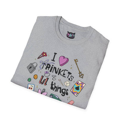 Gray T-shirt with "I love trinkets & lil things" text, featuring illustrations of a key, lock, dice, and colorful items, conveying a whimsical tone.