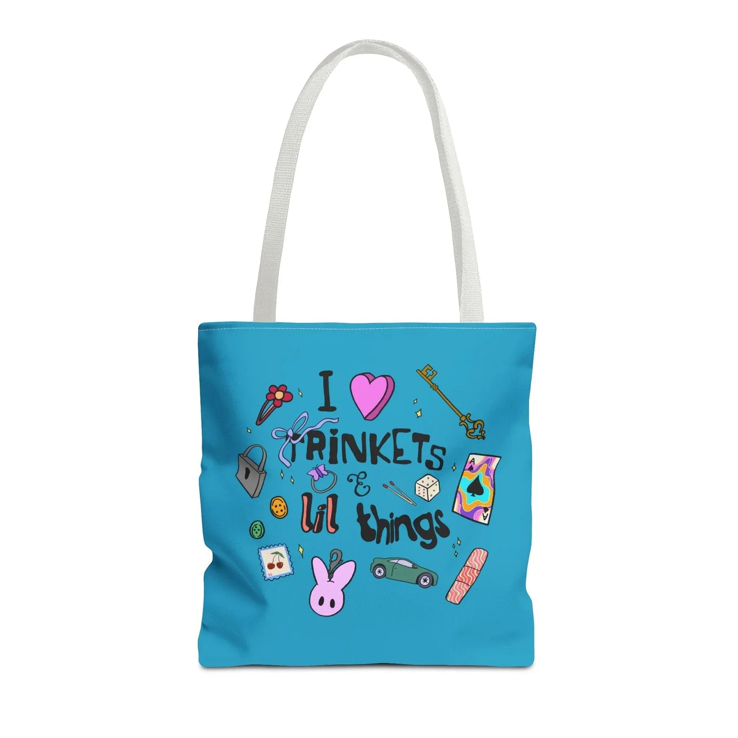 Blue tote bag with white handles, featuring playful doodles like a key, ribbon, dice, and cartoon bunny. Text reads "I love trinkets & lil things." Fun and whimsical.