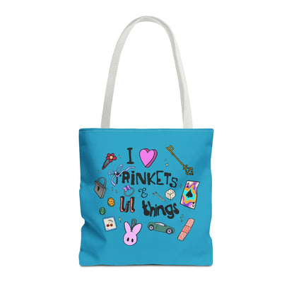 Blue tote bag with white handles, featuring playful doodles like a key, ribbon, dice, and cartoon bunny. Text reads "I love trinkets & lil things." Fun and whimsical.