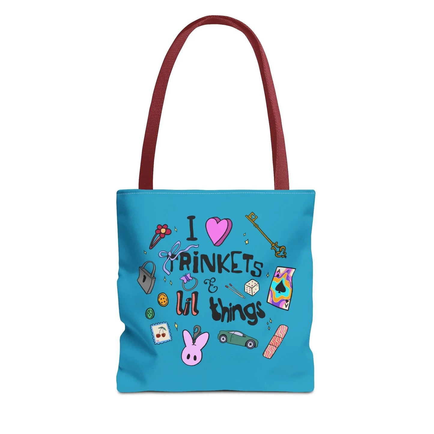 Blue tote bag with red handles, featuring playful doodles like a key, ribbon, dice, and cartoon bunny. Text reads "I love trinkets & lil things." Fun and whimsical.
