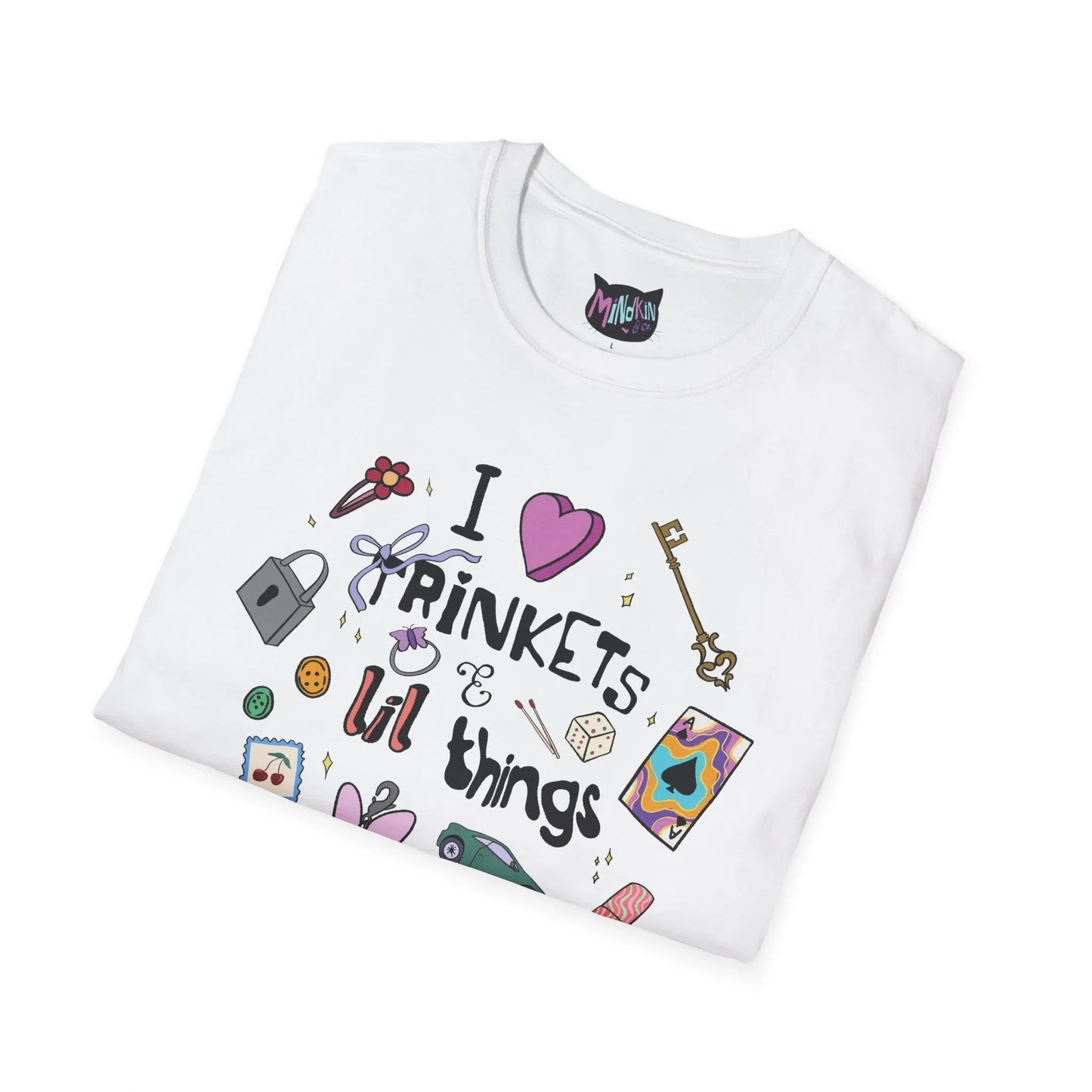 White T-shirt with "I love trinkets & lil things" text, featuring illustrations of a key, lock, dice, and colorful items, conveying a whimsical tone.