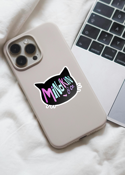 Smartphone with a white case featuring a Mindkin and Co. sticker on the back, next to an open laptop.