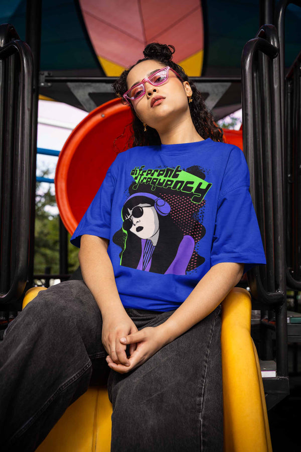 Young woman on a playground slide wearing pink sunglasses and a royal blue Different Frequency T-shirt. She exudes a cool and relaxed vibe.