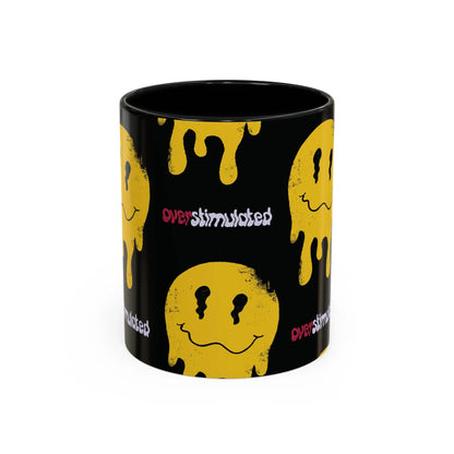 Side of black mug featuring yellow melting smiley faces and the word "overstimulated" in mixed red and white text. The design conveys a sense of playful chaos.